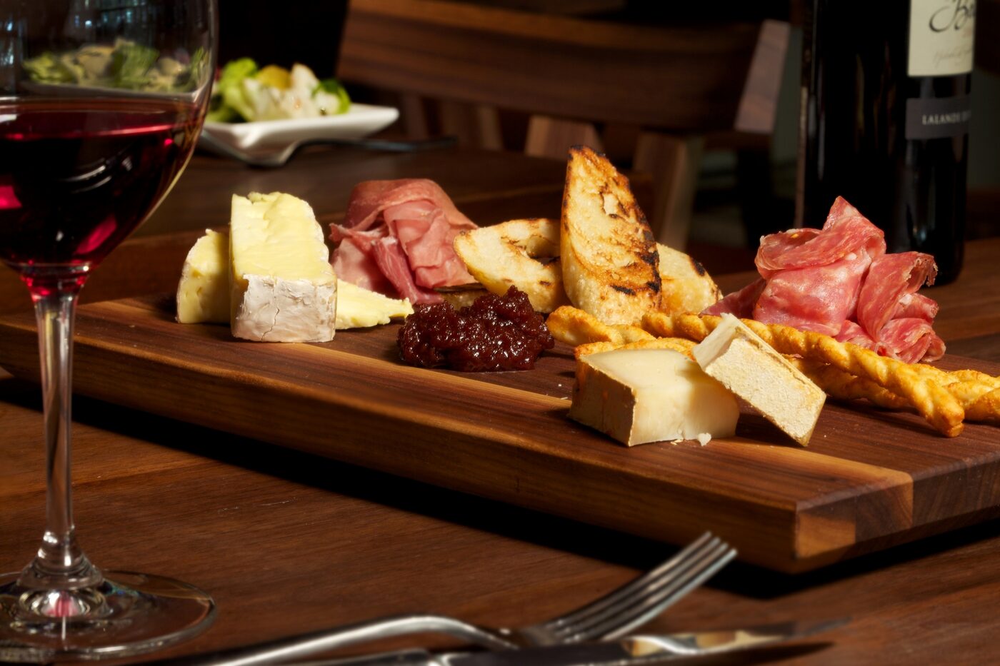Charcuterie board with cheese, cured meats, marmalade and grilled bread alongside a glass of red wine